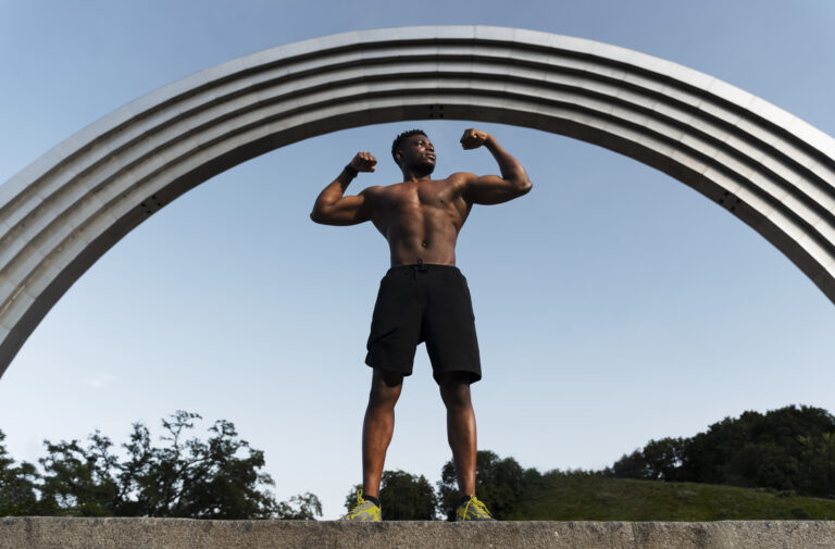 a man flexing his muscles under a arch, demonstrating achievement through positive mindset